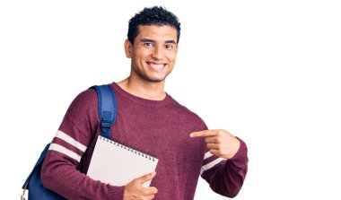 Sırt çantası ve not defteri takmış İspanyol yakışıklı genç adam gülümseyen ve gururlu birini işaret ediyor. 