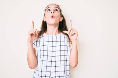 Hoş İspanyol çocuk gündelik giysiler giyip şaşkın şaşkın yukarı bakıyor ve parmaklarıyla işaret ediyor ve kollarını kaldırıyor.. 