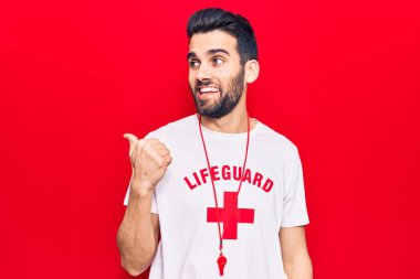 Sakallı, cankurtaran tişörtü giyen ve ıslık çalan genç yakışıklı bir adam baş parmağını kaldırıp gülümsüyor ve ağzı açık. 