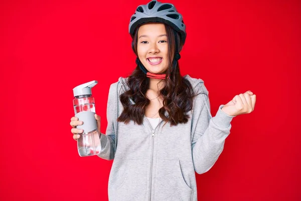 若い美しい中国の女の子は自転車のヘルメットを身に着けていると誇りに思って叫んで水ボトルを保持 勝利と成功を祝う非常に腕を上げ興奮 — ストック写真