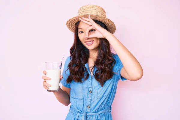年轻美丽的中国姑娘戴着夏帽 手里拿着一杯牛奶 开心地微笑着 手拿着手签 用手指看过去 — 图库照片