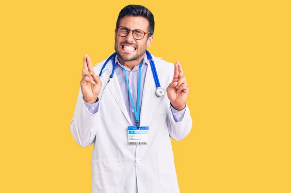 Jovem Hispânico Vestindo Uniforme Médico Estetoscópio Gesticulando Dedo Cruzado Sorrindo — Fotografia de Stock