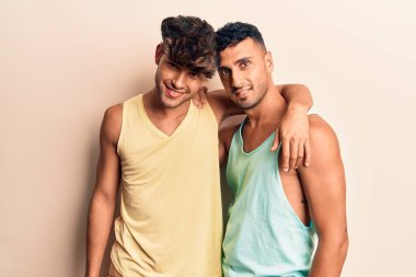 Yazlık kıyafetler giyen genç bir çift mutlu gülümsüyor. Yüzünde gülümsemeyle dikilip izole edilmiş beyaz arka planda sarılıyorum.