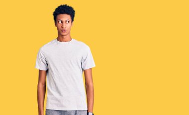 Genç Afro-Amerikan adam günlük kıyafetler giyiyor gülümsüyor yan tarafa bakıyor ve düşünüyor. 