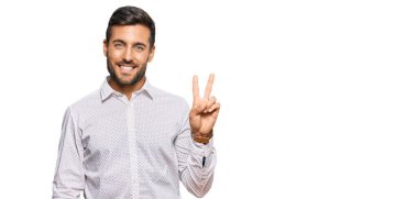 İş kıyafetleri giymiş yakışıklı İspanyol bir adam kameraya gülümseyen bir gülümsemeyle zafer işareti yapıyor. İki numara.. 