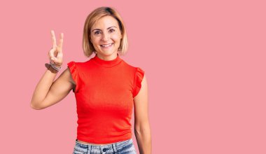 Gündelik kıyafetler giyen genç sarışın kadın iki numarayı gösterip işaret ederken kendine güvenen ve mutlu bir şekilde gülümsüyor.. 