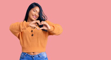 Uzun saçlı, sıradan bir kazak giyen, aşık gülümseyen, elleriyle kalp sembolü yapan İspanyol bir kadın. romantik kavram. 