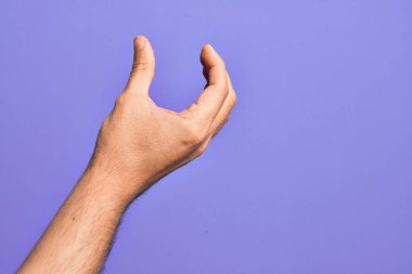 İzole edilmiş mor arka plan üzerinde parmaklarını gösteren beyaz bir adamın eli. Görünmez bir şeyi alıyor, parmakları boşluğu gösteren bir nesneyi tutuyor.