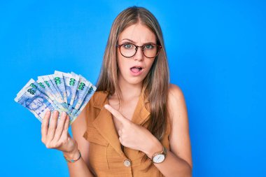 Güney Afrika Rand banknotlarını elinde tutan genç sarışın kız, şaşkın ve alaycı görünüyor, ağzı açık kalınca şaşırıyor. 