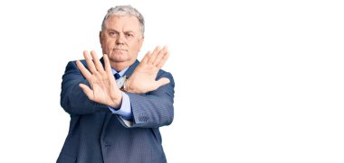 İş ceketi giyen yaşlı gri saçlı adam. Reddedilmiş yüz ifadesi. Kollarını kavuşturup, avuçlarını çaprazlayarak negatif işaret veriyor. 