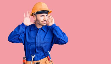 İşçi üniforması giyen genç İspanyol adam iki elini de kulak hareketine koyup dedikoduya meraklı olmaya çalışıyor. İşitme sorunu, sağır 