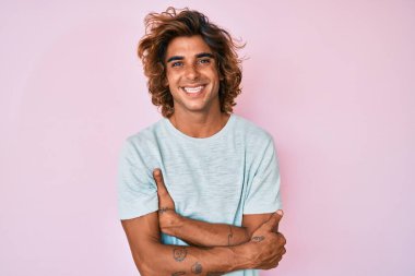 Gündelik kıyafetler giyen, kollarını kavuşturup kameraya gülümseyen genç İspanyol adam. pozitif kişi. 