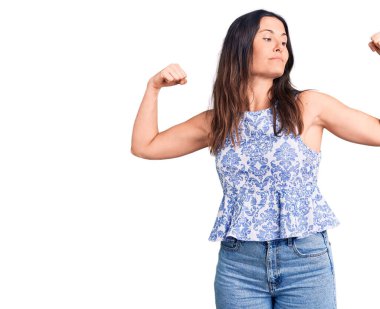 Genç, güzel, esmer bir kadın, sıradan tişörtler giyip, gururla gülümseyen kol kaslarını gösteriyor. fitness konsepti. 