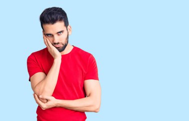 Sakallı, sıradan tişörtlü, yorgun görünen ve depresyondan sıkılmış kolları çaprazlanmış genç yakışıklı bir adam.. 