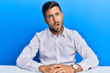 Yakışıklı, iş kıyafetleri giyen, şok olmuş bir halde masada oturan, şüpheci ve alaycı bakışlı, ağzı açık bir şekilde şaşırmış biri. 