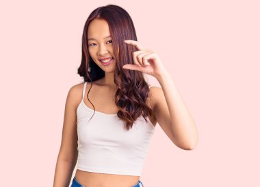 Genç, güzel Çinli bir kız, günlük kıyafetler giymiş, gülümseyen, kendine güvenen, el hareketi yapan, parmaklarıyla işaret yapan ve kameraya bakan. ölçüm kavramı. 