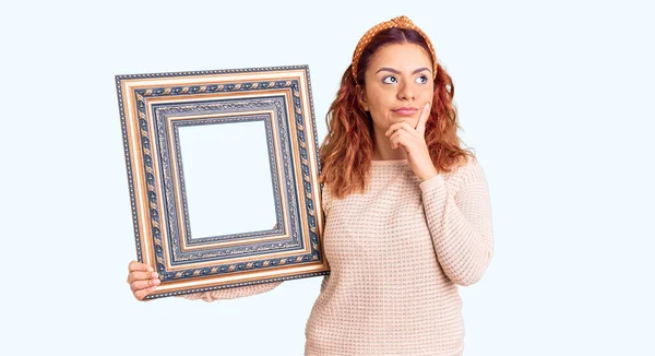Young Latin Woman Holding Empty Frame Serious Face Thinking Question — Stock Photo, Image