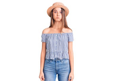 Şapka ve tişört giyen güzel bir kız komik yüzüyle yanaklarını şişiriyor. Havayla şişmiş ağız, çılgın bir ifade.. 