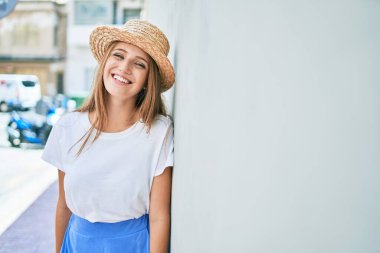 Genç sarışın kadın tatilde gülümsüyor. Mutlu bir şekilde şehrin duvarına yaslanıyor.