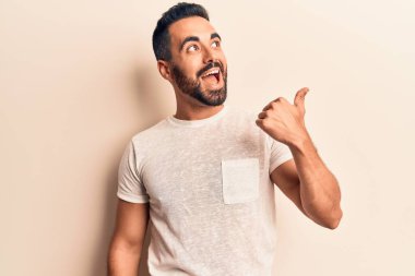 Gündelik giysiler giymiş genç İspanyol bir adam baş parmağını yana kaldırıyor ve ağzı açık gülümsüyor. 