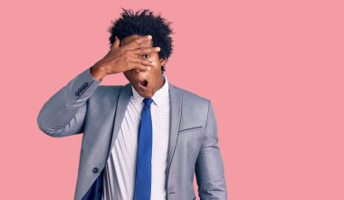 Yakışıklı Afro saçlı, iş ceketi giyen, yüzü ve gözlerini kapayarak utangaç ifadesiyle parmaklarından içeri bakan afro-amerikalı bir adam.. 