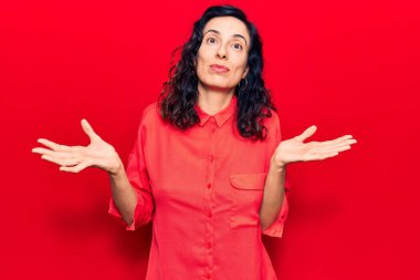 Gündelik kıyafetler giyen, kafası karışmış, elleri ve kolları havada, genç ve güzel İspanyol bir kadın. şüphe kavramı. 