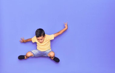 Hoş bir çocuk, günlük giysiler içinde izole edilmiş mor bir arka planda zıplıyor.