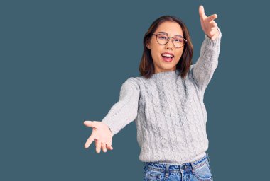 Gündelik giysiler giymiş genç, güzel Çinli bir kız kameraya bakıyor ve sarılmak için kollarını açmış gülümsüyor. Mutluluğu kucaklayan neşeli bir ifade.. 