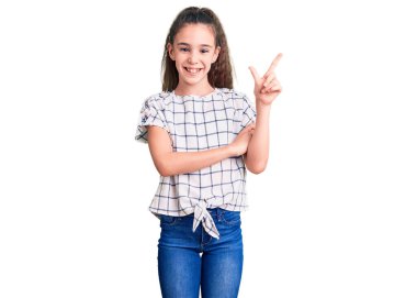 Yüzünde kocaman bir gülümseme olan, gündelik kıyafetler giyen, eli ve parmağı kameraya bakan tatlı İspanyol kız çocuğu.. 