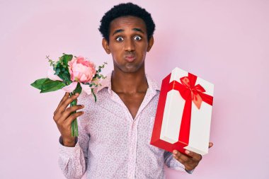 Yıldönümü hediyesi tutan Afrikalı yakışıklı bir adam ve komik suratlı bir buket çiçek şişiren yanaklar. Ağzı havayla şişer, havayı yakalar.. 