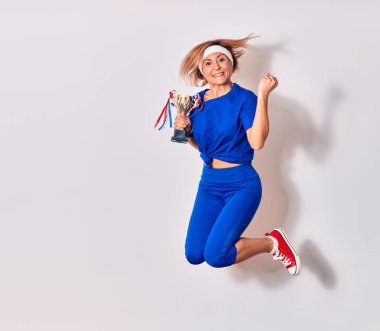 Genç beyaz kadın spor giyer, mutlu bir şekilde gülümser. İzole edilmiş beyaz arka planda yüzünde gülümsemeyle zıpla