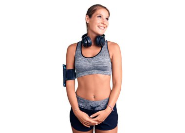 Spor kıyafetleri giyen, kulaklık takan, yüzünde gülümseme, doğal bir ifade olan genç, İspanyol bir kadın. Kendinden emin gülen. 