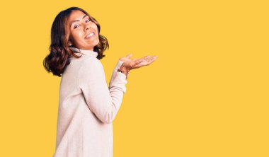 Balıkçı yaka kazak giyen genç, güzel, melez bir kadın. Avuç içleri açık, fotokopi alanını gösteriyor. Gülümseyen, mutlu bir gülümseme reklamı veriyor. 