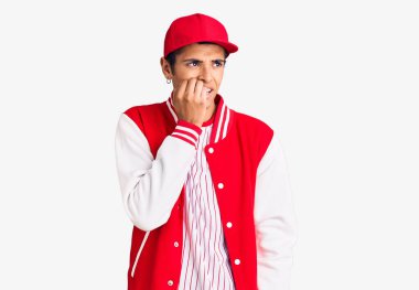 Beyzbol üniforması giyen Afrikalı genç bir Amerikalı. Elleri ağız ısıran, gergin ve stresli görünüyor. anksiyete. 