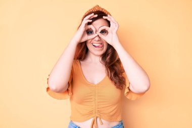 Genç ve güzel bir kadın günlük kıyafetler giyip dürbün gibi jest yapıyor, gözleri parmaklarından bakıyor. çılgın ifade. 