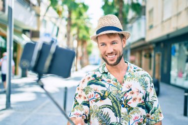 Beyaz tenli yakışıklı adam mutlu bir şekilde dışarıda selfie çekiyor. Selfie çubuğu kullanıyor.