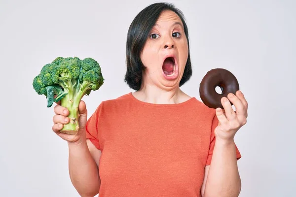 Mujer Morena Con Síndrome Sosteniendo Brócoli Donut Chocolate Asustado Sorprendido — Foto de Stock