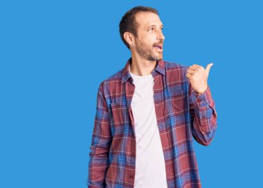 Genç, yakışıklı, sıradan kıyafetler giyen, gülen yüzlü, gülümseyen ve baş parmağıyla yan tarafı gösteren bir adam.. 