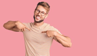 Gündelik kıyafetler ve gözlük takan, kendine güvenen, gülümseyen, kendini gururlu ve mutlu gösteren genç beyaz bir adam.. 