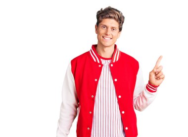 Beyzbol üniforması giyen, yüzünde kocaman bir gülümseme olan genç ve yakışıklı bir adam, kameraya el ile işaret ediyor.. 