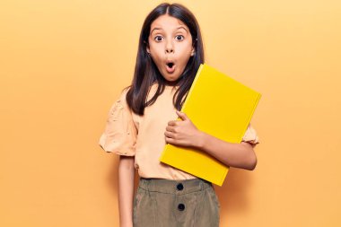 Güzel kız elinde kitap tutuyor. Korkmuş ve şaşırmış bir şekilde ağzı açık, şaşırmış bir halde. 