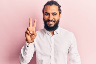 Gündelik giysiler giyen genç Arap adam iki numarayı gösterip işaret ederken kendinden emin ve mutlu gülümsüyor.. 