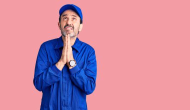 Orta yaşlı yakışıklı bir adam mekanik üniforması giyiyor. Elleriyle yalvarıyor ve dua ediyor. Yüzünde umut ifadesi var. Yalvarıyor. 