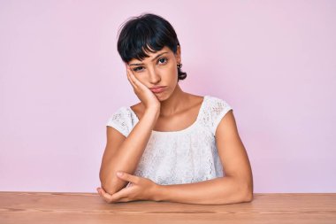 Güzel esmer kadın pembe arka plan üzerine günlük kıyafetler giyip kollarını kavuşturarak depresyondan sıkılmış ve yorgun görünüyor.. 