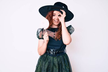 Cadı cadılar bayramı kostümü giyen genç ve güzel bir kadın elinde lolipop tutarak gülümsüyor. 