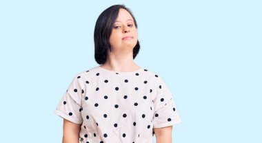 Down sendromlu esmer kadın rahat kıyafetler giyiyor ve yüzünde ciddi bir ifade var. Basit ve doğal bir şekilde kameraya bakıyorsun.. 