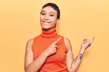 Gündelik kıyafetler giyen, gülümseyen ve kameraya bakan genç bir kadın iki eliyle ve parmaklarıyla kenarı işaret ediyor.. 