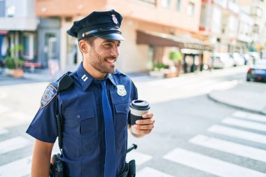 Polis üniforması giyen genç İspanyol polis mutlu bir şekilde gülümsüyor. Kasaba caddesinde dikilmiş kahve içerken.