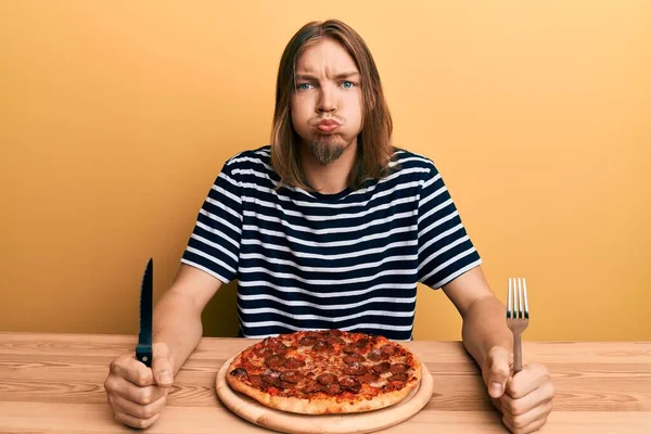 英俊的白种人 吃着美味的意大利辣披萨 脸上带着滑稽的表情 嘴被空气吹胀 — 图库照片
