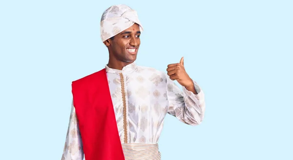 アフリカのハンサムな男身に着けている伝統的なSherwani見た服笑顔で幸せな顔を見て 親指で側面を指してアップ — ストック写真